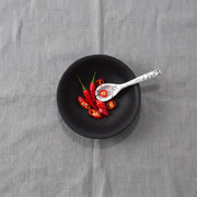 POLKA LUKA matte black resin relish bowl with a white marble-effect spoon containing sliced red chili peppers