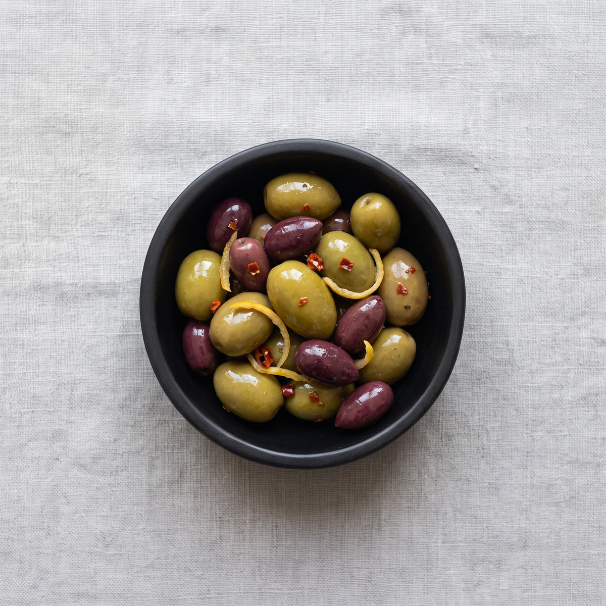 POLKA LUKA small black resin Luna bowl filled with green and purple olives on a textured linen tablecloth